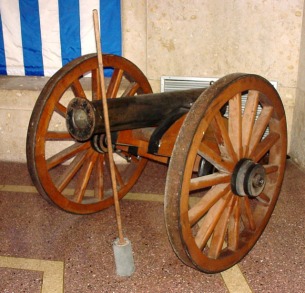 Replica cannon (a) with wooden ramrod (b), swab (c), and copper bucket (d). Identical to c2.a-d.